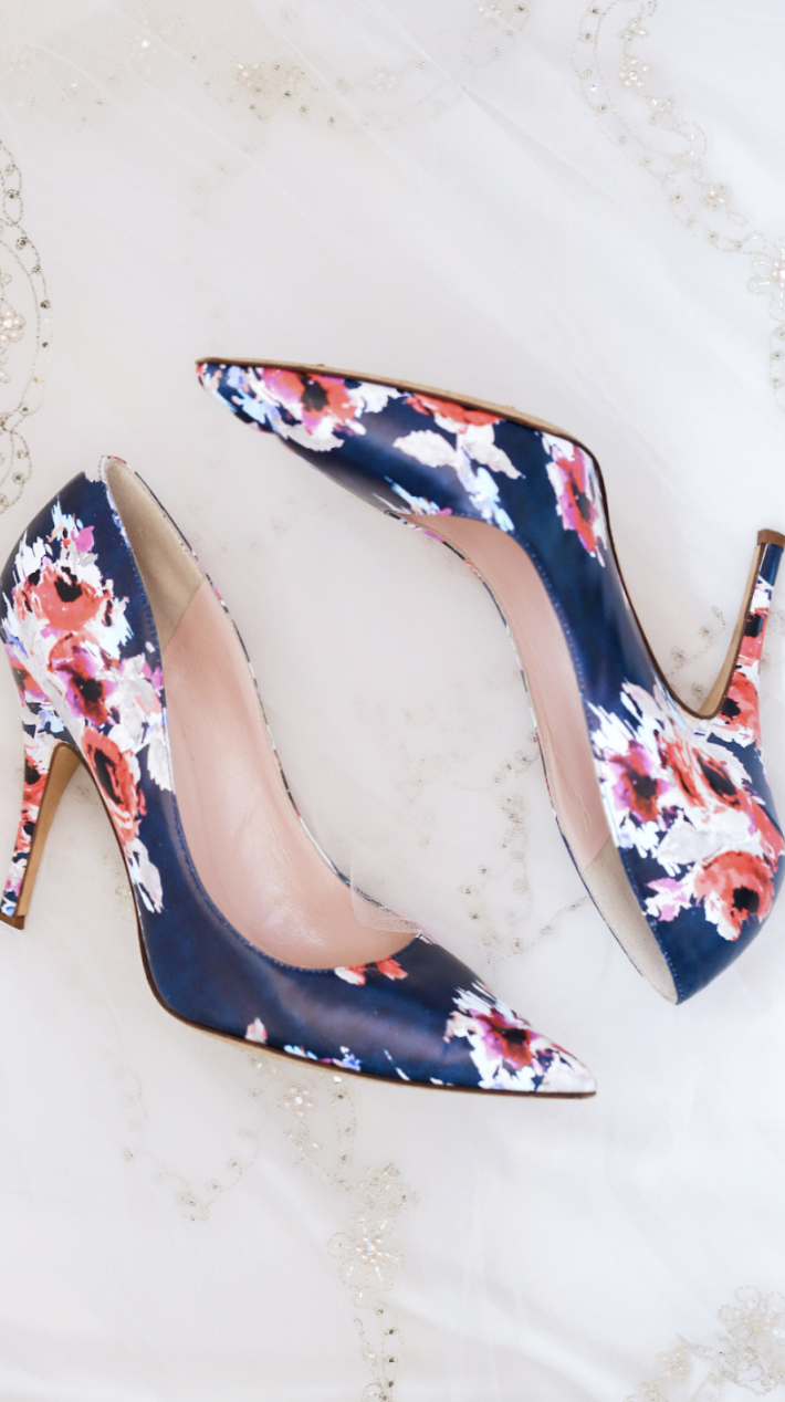 Women’s Pumps with four-inch heels and floral print on navy blue background laying on a marble surface